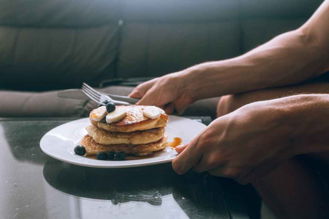 person holding white plate with pancakes